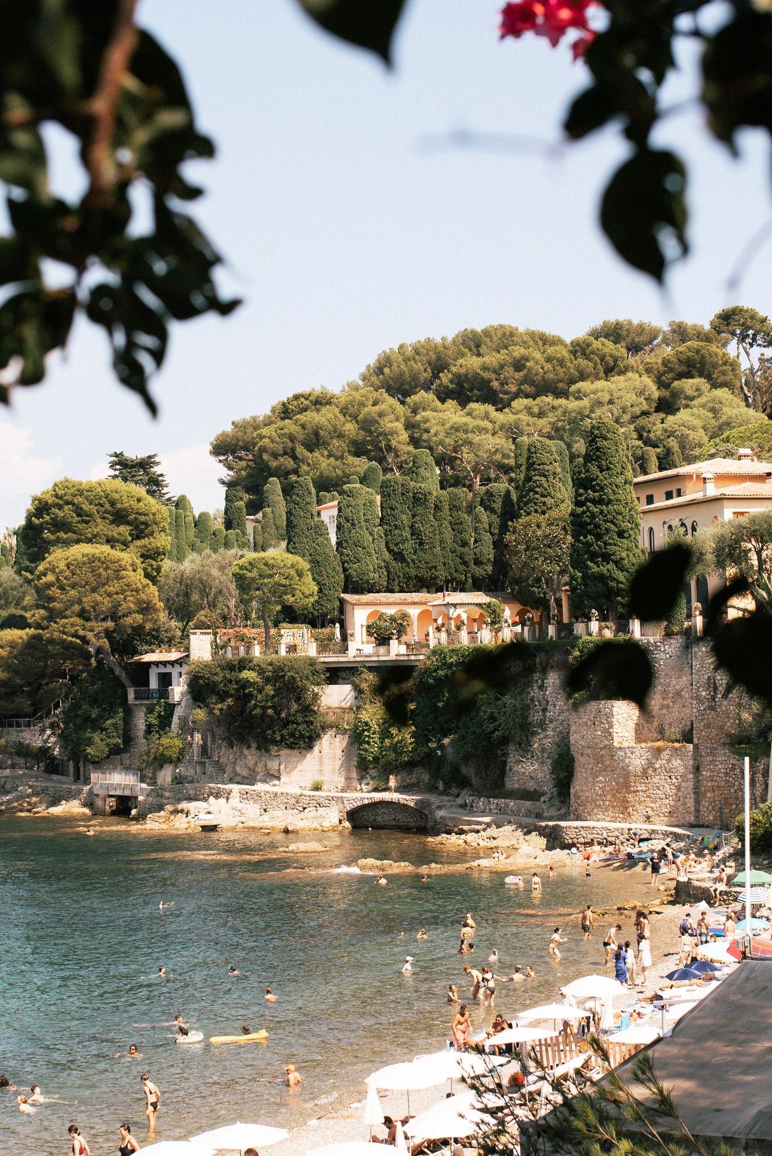 A small white wooden boat moored in calm clear waters near a hillside Mediterranean village.