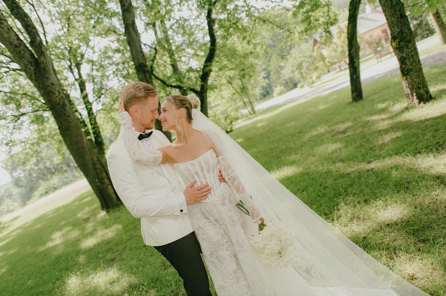 Bride and groom share a romantic moment under lush green trees in an outdoor wedding photo.