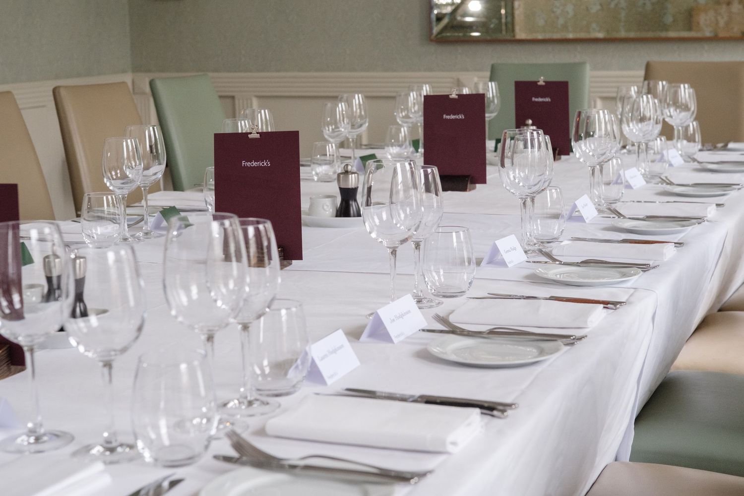 Elegantly set long dining table with white tablecloth, crystal wine glasses, and maroon menus for a formal event.