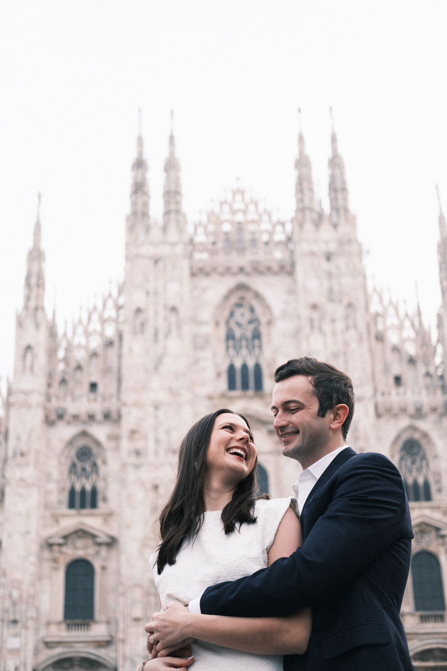 A joyful couple embraces and laughs in front of the Milan Cathedral, Duomo di Milano, Italy.
