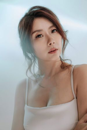Close-up portrait of a beautiful Asian woman in white camisole with soft lighting and natural makeup.