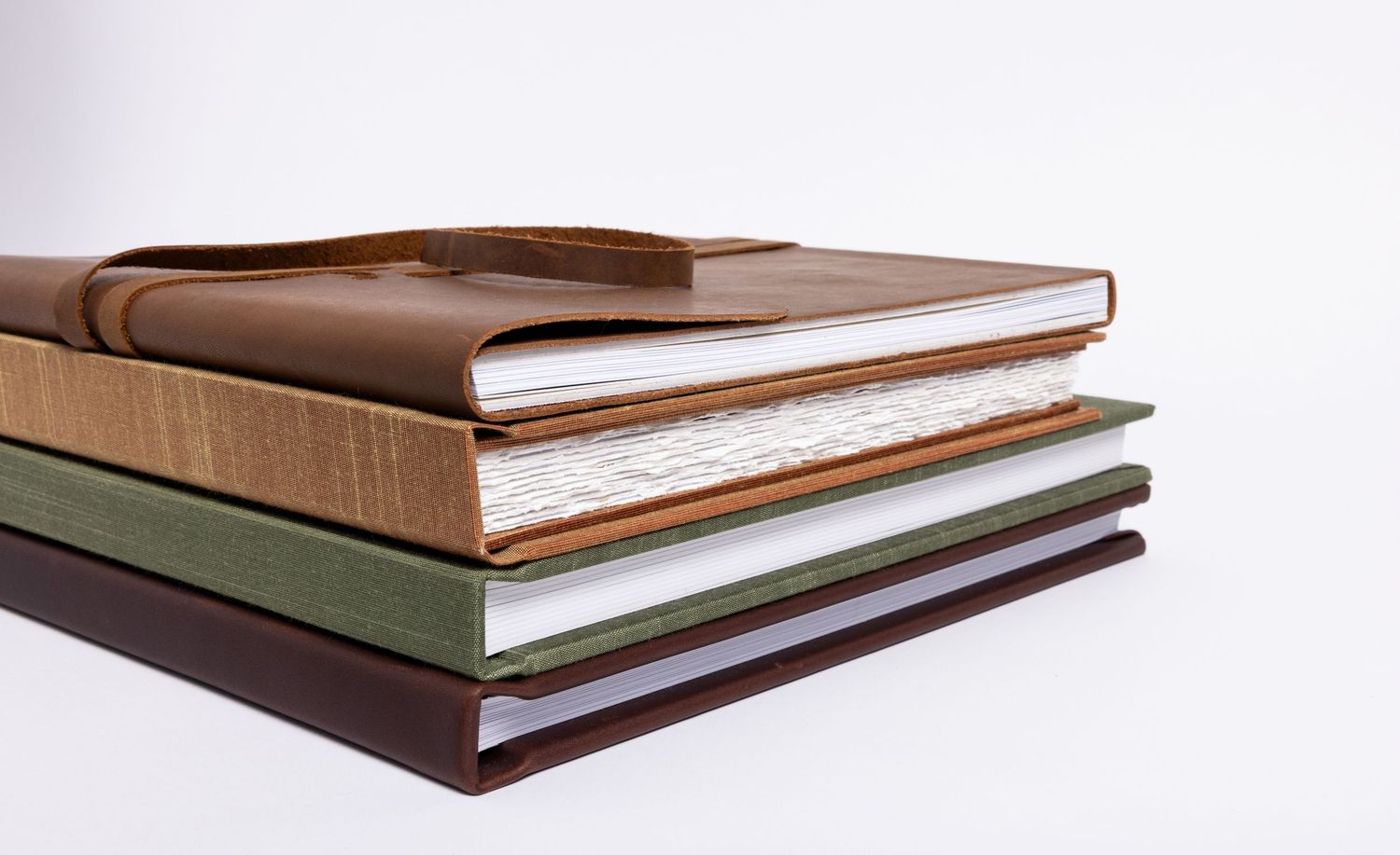Stack of custom photo albums of people's pets in leather, silk, and linen fabric.