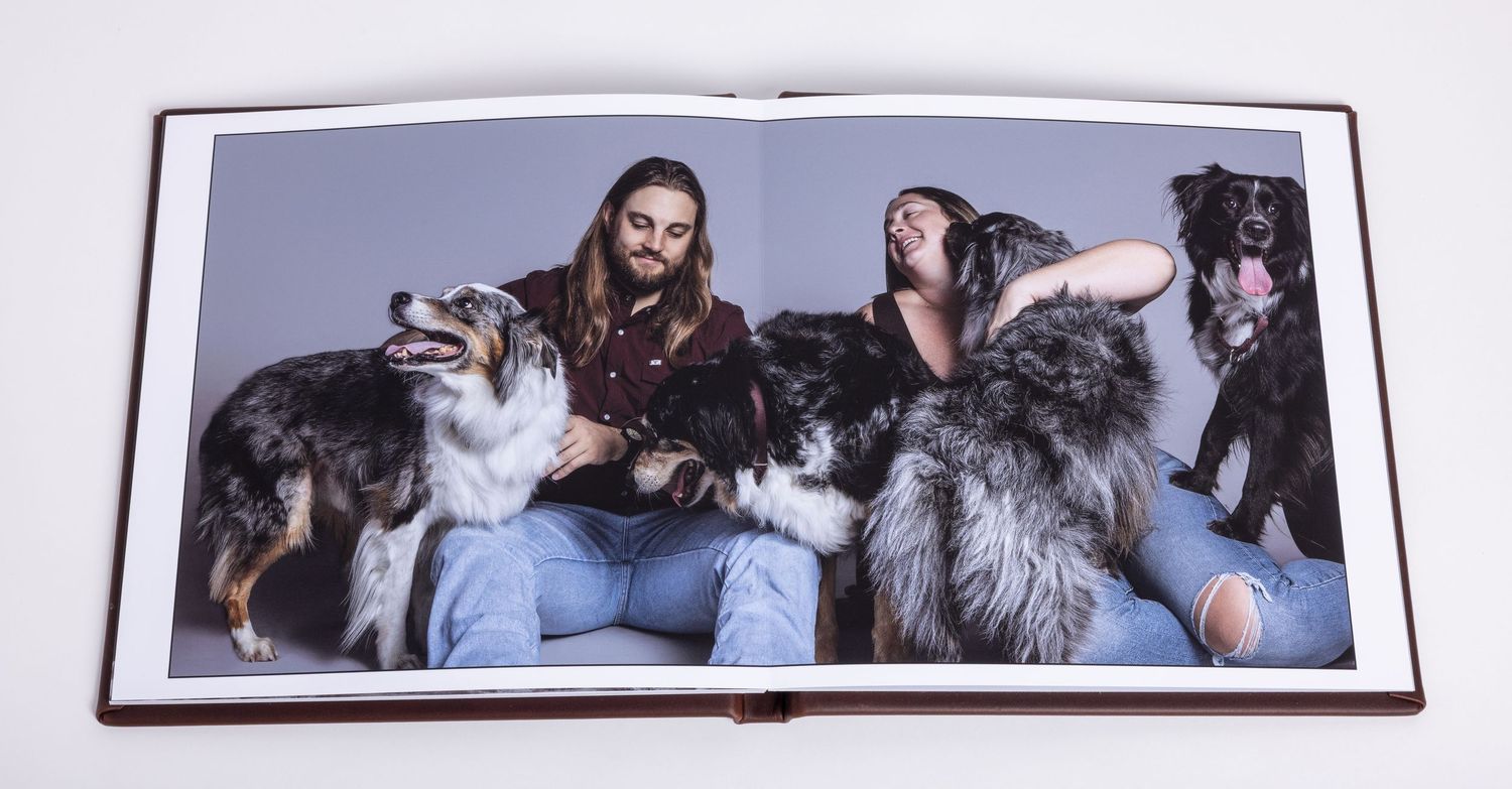 Open photo album created by an Austin pet photographer showing two people sitting with five large fluffy dogs.