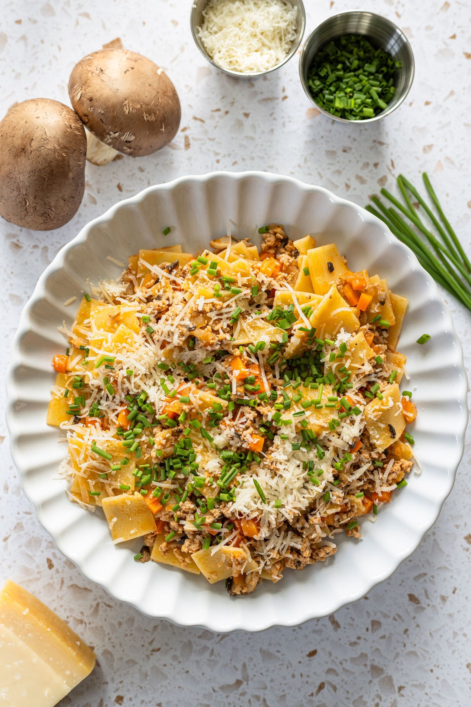 Pappardelle pasta with meat sauce, parmesan, chives, mushrooms, and fresh herbs in a white bowl.