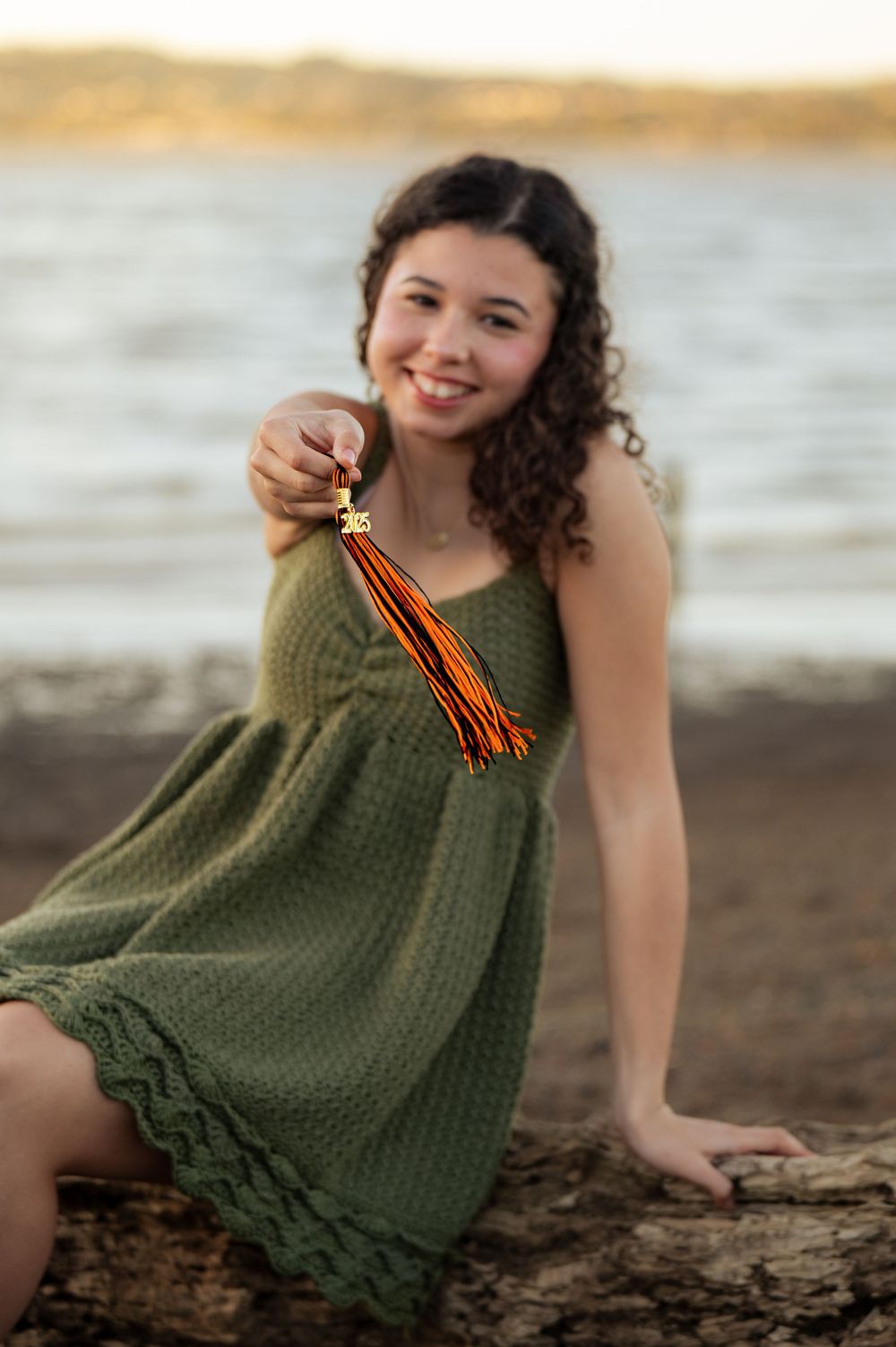 Person wearing an olive green crochet dress sits on a beach during golden hour.