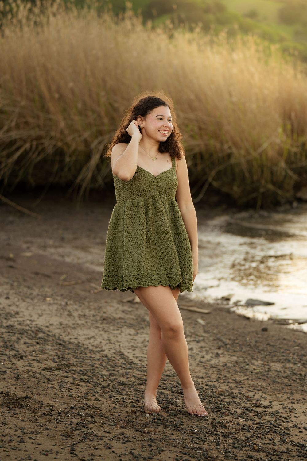 Candid beach photoshoot featuring someone in a green knit dress against tall grass.