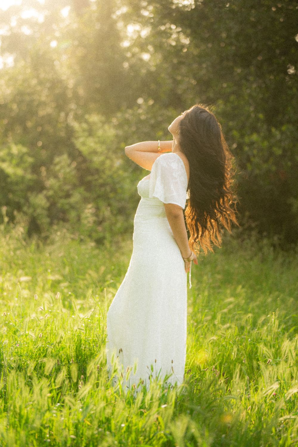 Ethereal white dress catches sunlight in a verdant meadow during golden hour.