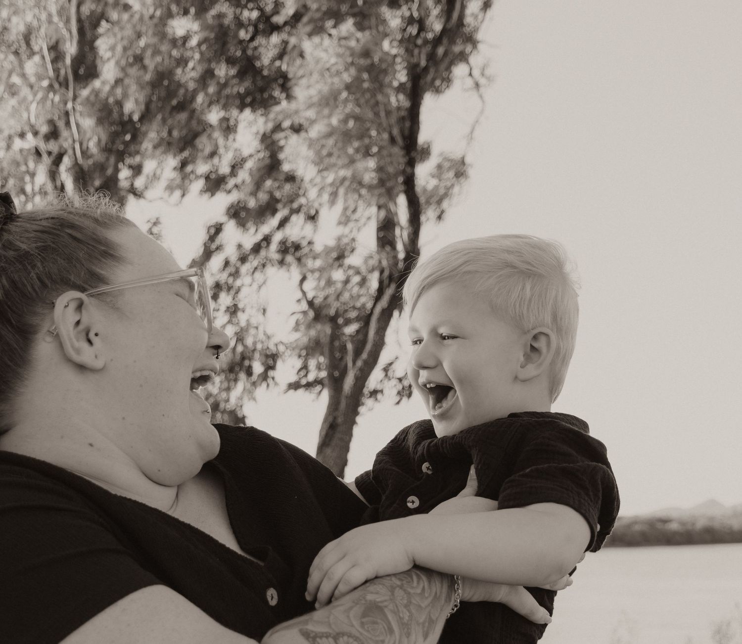 Mother laughing joyfully while holding her giggling toddler son in a black and white outdoor photo.