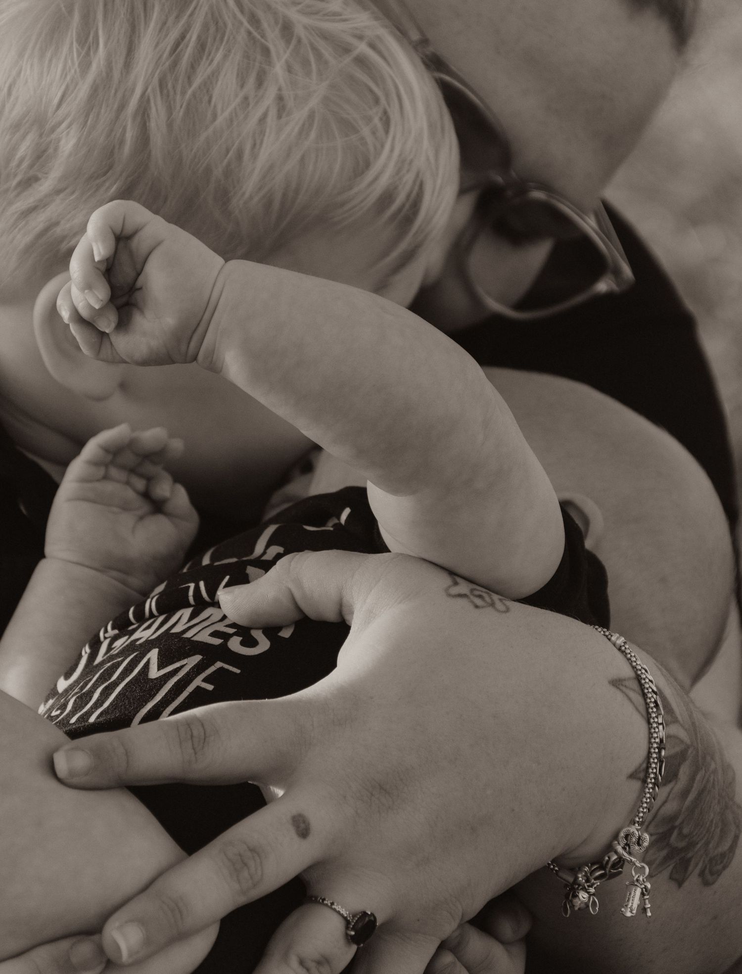 Close-up black and white photo of a tattooed mother tenderly cradling her sleeping newborn baby.