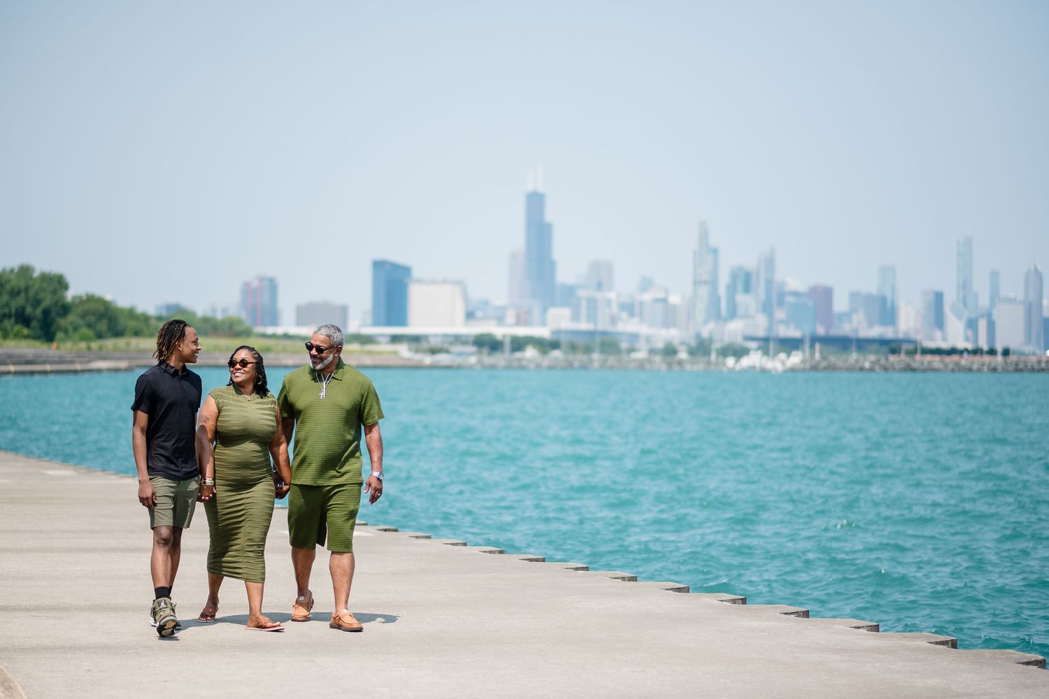 Three people walking along a lakefront path with the Chicago skyline in the background on a sunny day.