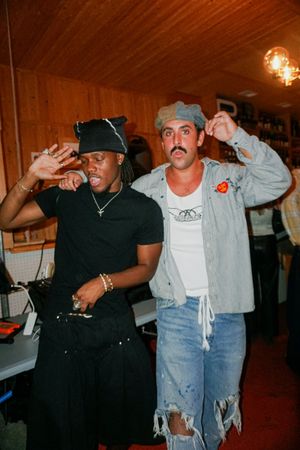 Two men posing playfully in a cozy wood-paneled bar or music venue.