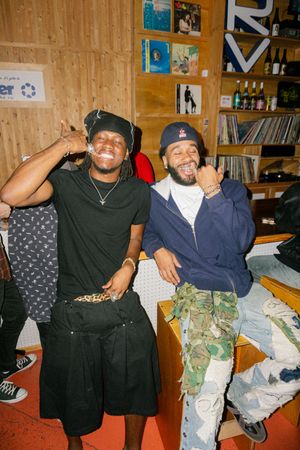 Two young men smiling and posing with shaka signs in a record shop.