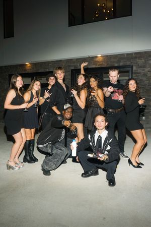 Group of young adults in black outfits posing together at an outdoor evening party event.