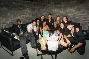 Group of young adults posing together on a couch at an indoor party with gifts on a table.