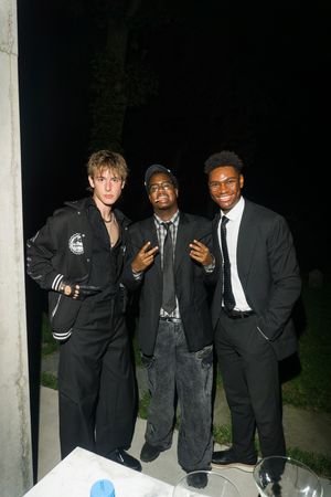 Three young men in black outfits posing together at an outdoor nighttime event.
