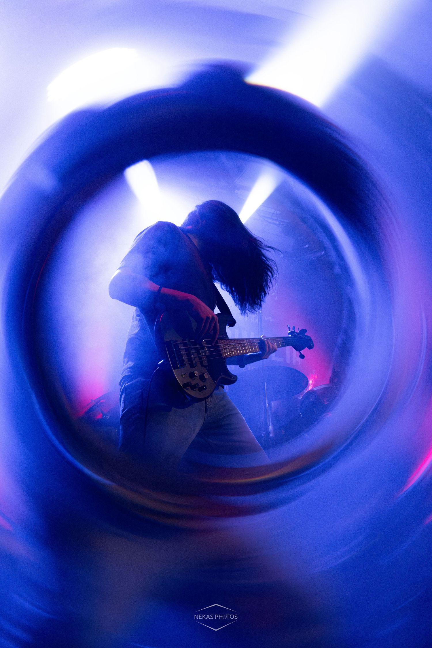 Guitarist performing on stage under dramatic blue and purple lights, captured through a circular lens effect.