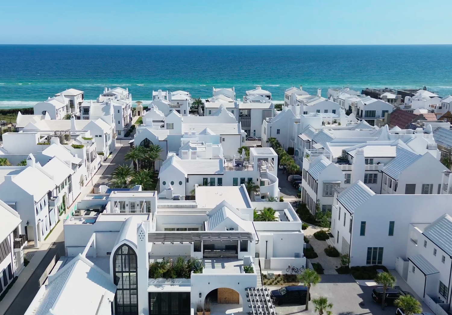 Aerial view of white coastal homes and villas near turquoise ocean waters in a sunny beach community.