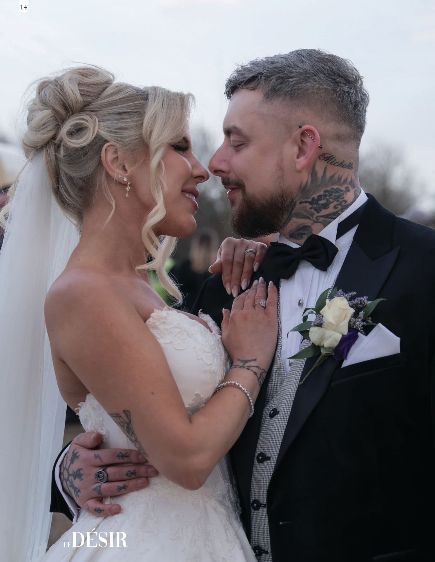 Tattooed bride and groom in tuxedo sharing romantic moment at outdoor wedding ceremony.