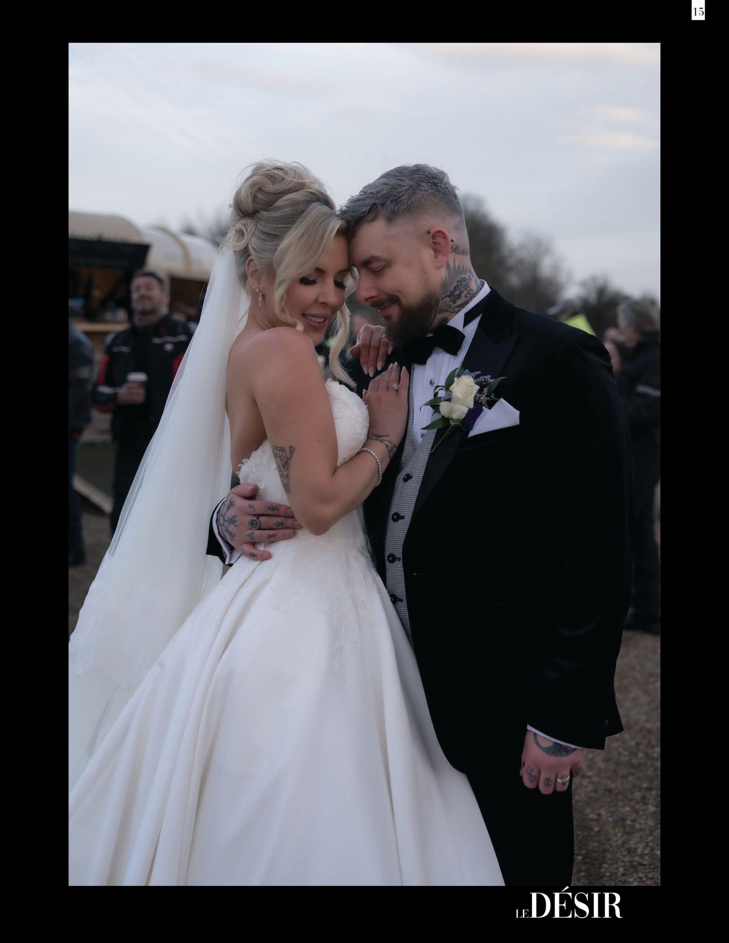 A bride and groom share an intimate moment outdoors, she in a white ballgown with veil, he in a black tuxedo.