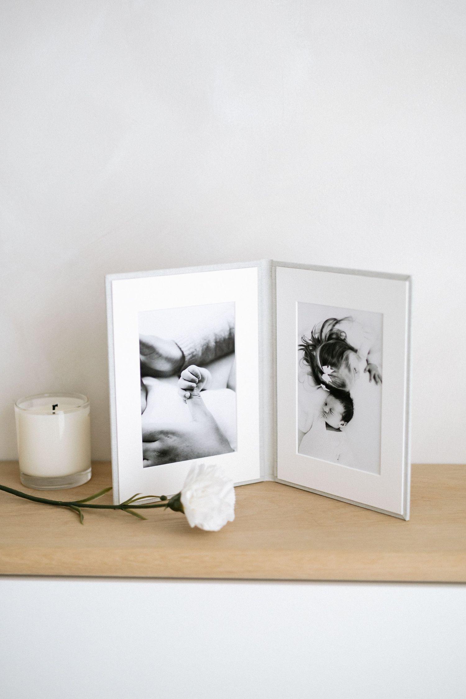 Black and white baby photos in a double frame on a wooden shelf with a white rose Nottingham natural newborn and family photographer