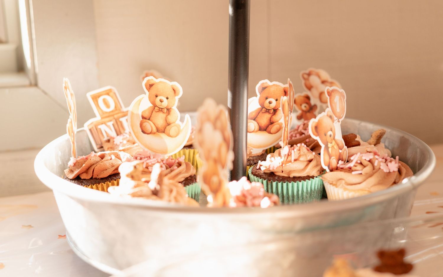 Cupcakes with teddy bear toppers on a tiered stand, decorated with pink frosting for a baby shower.
