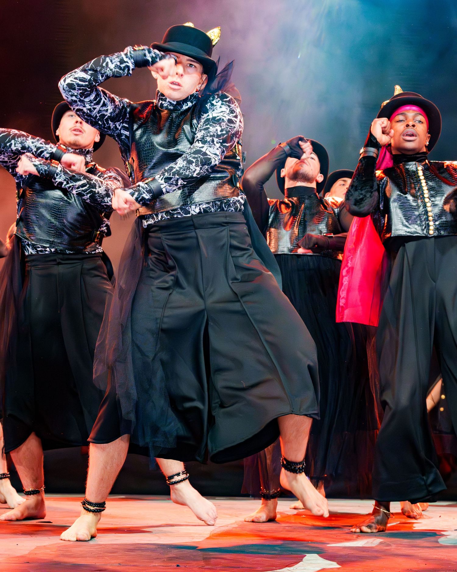 Male dancer in black pants and open jacket strikes an elegant arched pose against a gray studio background.
