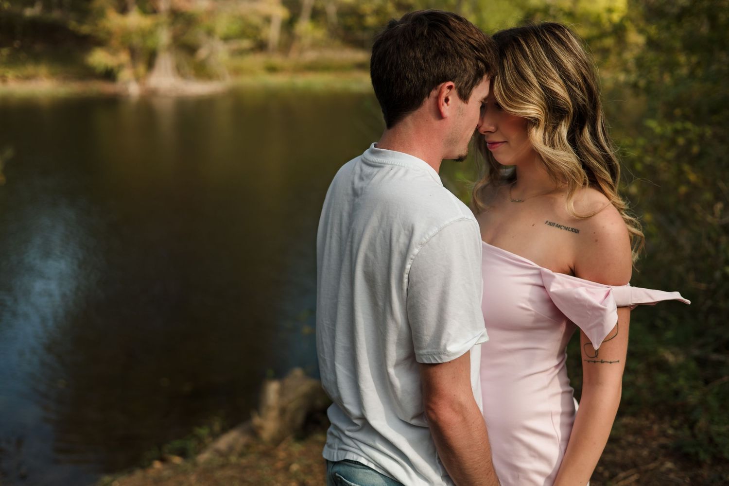 An intimate and natural "Love Stories" portrait of a couple embracing by a serene lakeside at sunset in Central Texas.