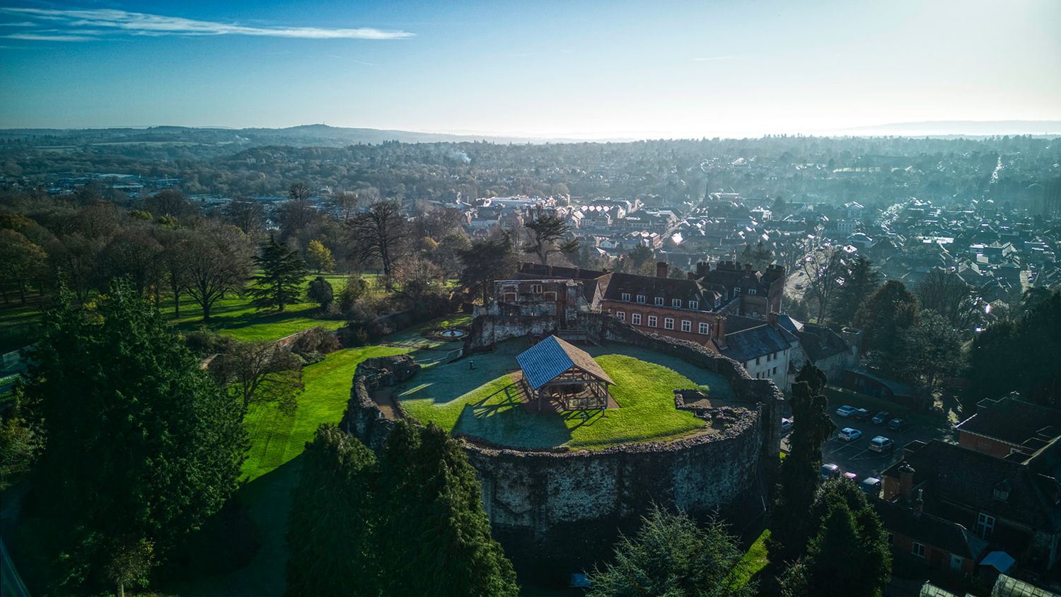 Aerial view of a historic castle with lush green gardens surrounded by a sprawling cityscape on a sunny day.