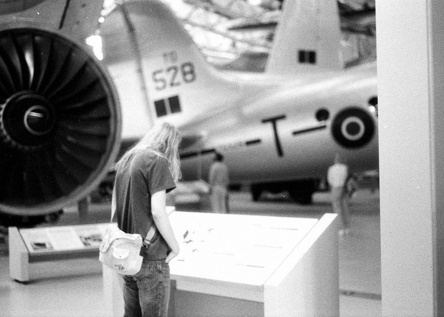 Person viewing aircraft exhibit at aviation museum with vintage military planes and large jet engine on display.