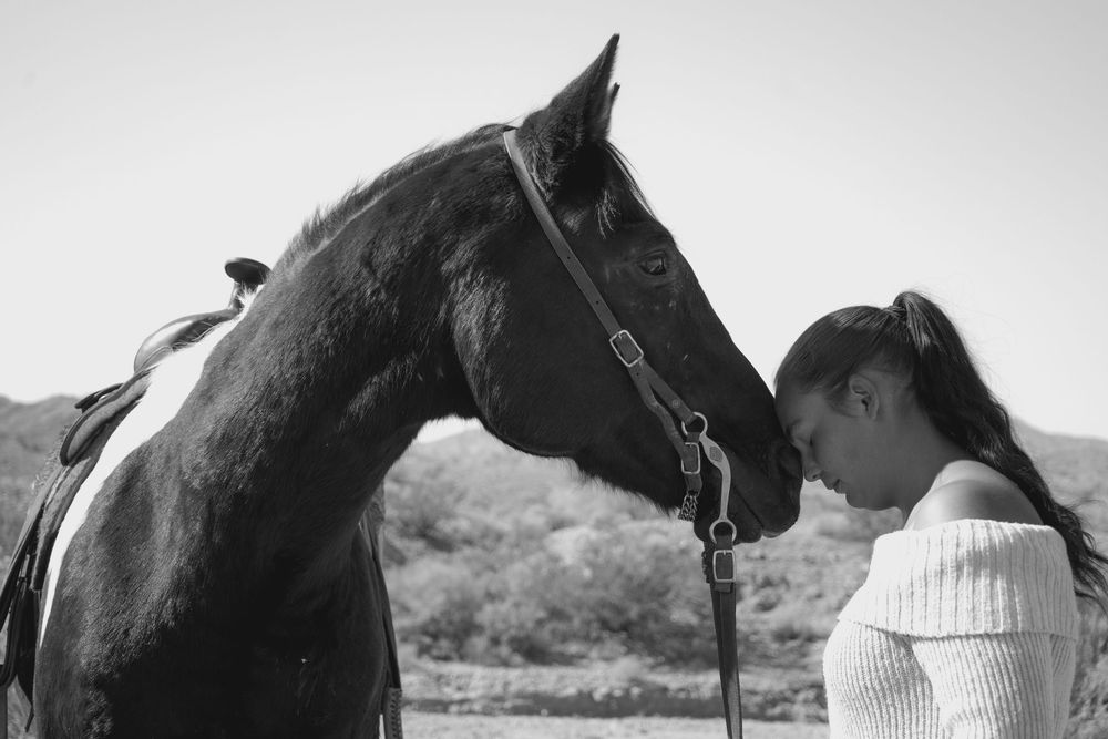 Black and white photo of a woman touching foreheads with a dark horse.