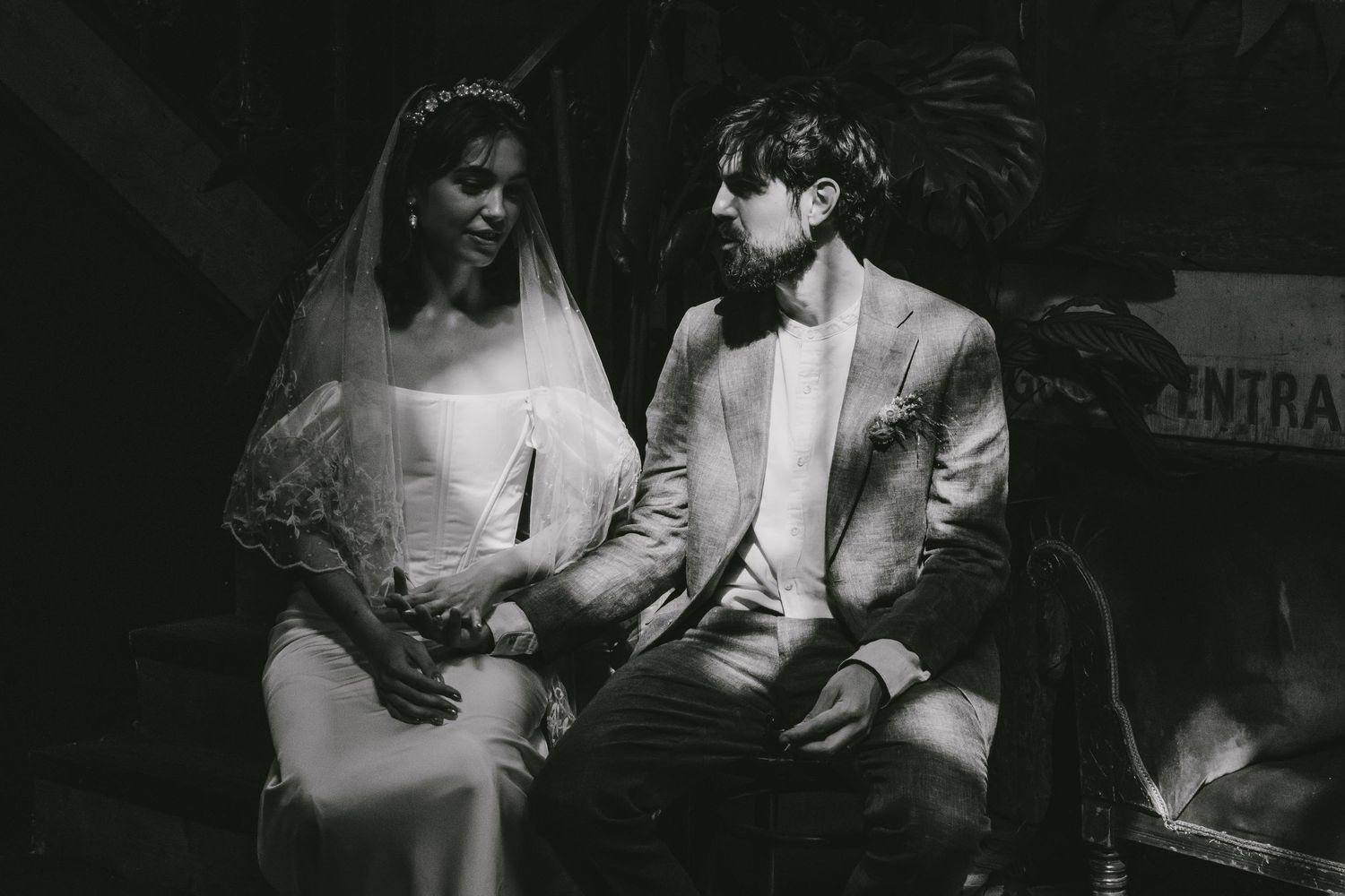 Black and white wedding photo of bride in veil and groom in suit sitting together at outdoor ceremony.