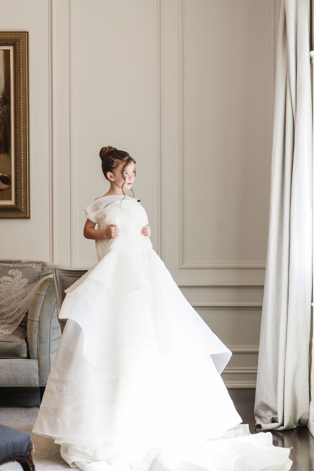 Young girl twirling in a white tiered ball gown in an elegant room with classic moldings and soft natural light.