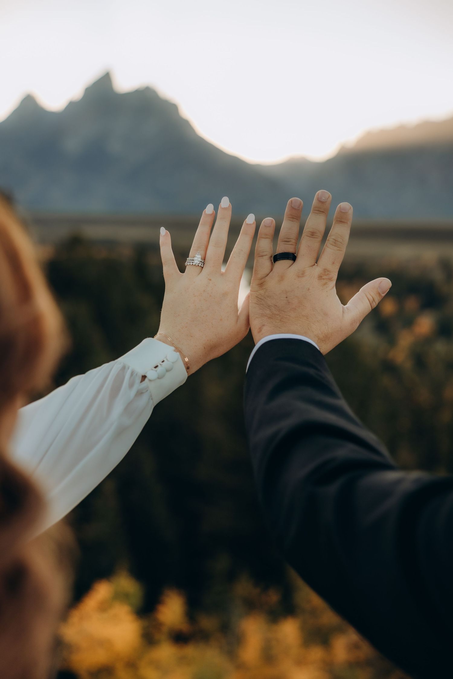 Two hands raised against a mountainous backdrop at sunset with fall foliage in the background.