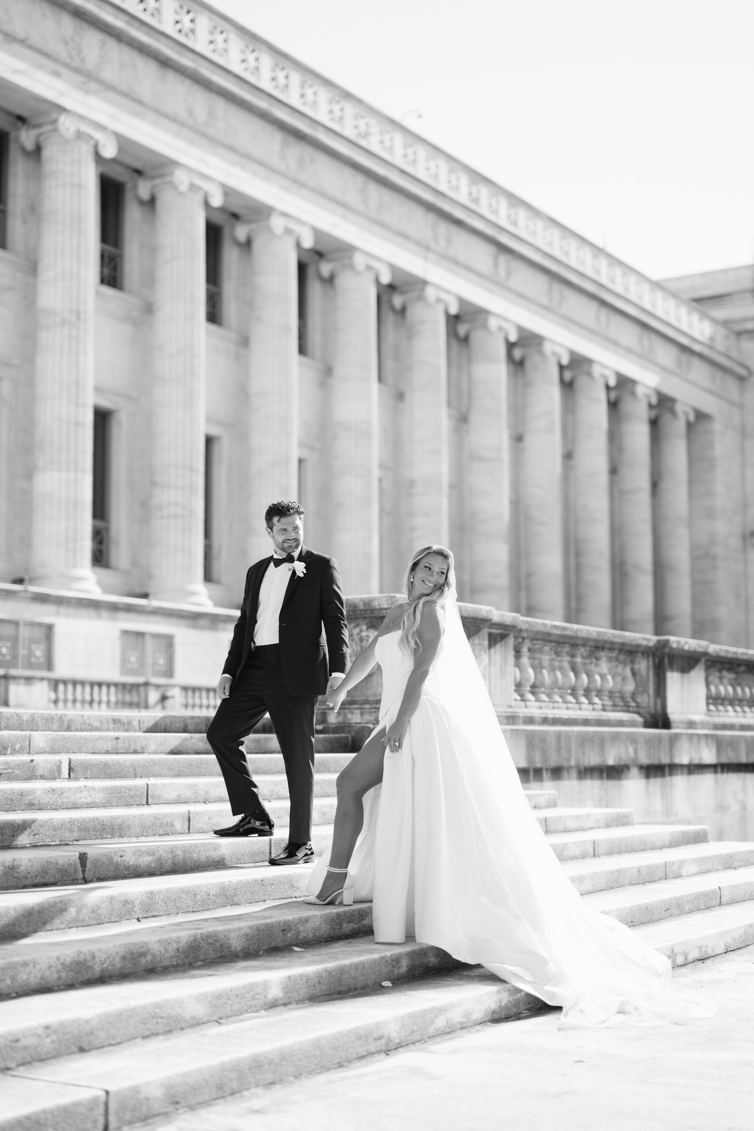 A romantic couple in wedding attire shares intimate moments on a manicured lawn in front of a grand stone building.