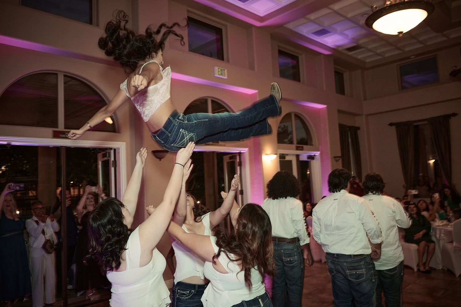 People dancing and celebrating at an indoor event venue with purple mood lighting and elegant decor.