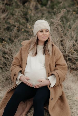 A person in a cozy beige cardigan and white sweater poses outdoors against a natural backdrop in a lifestyle photoshoot.