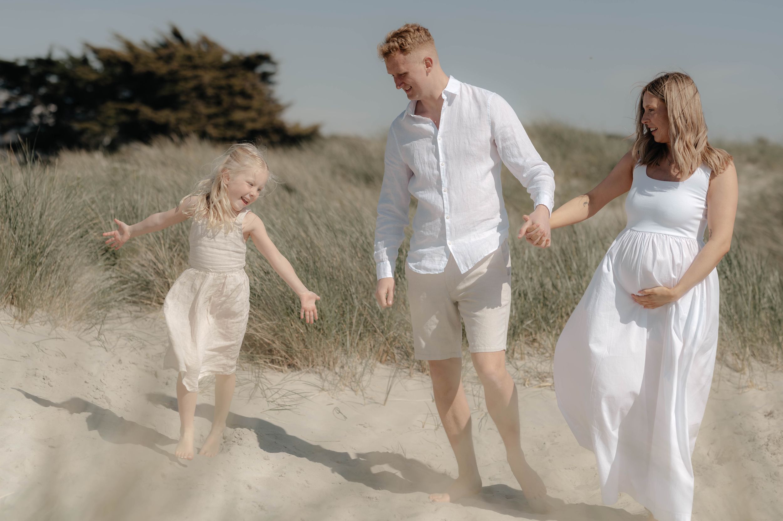 A group of people in white outfits playing and dancing together on a sandy beach during sunset.