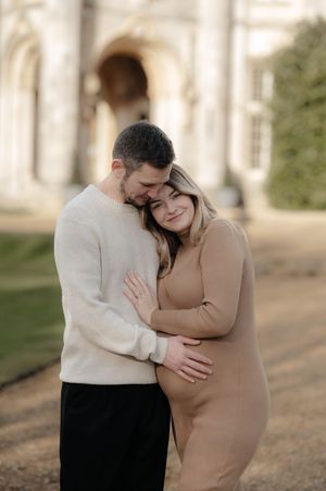 A couple embraces tenderly in an outdoor setting wearing contrasting beige and white outfits.