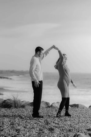 A black and white photo sequence showing a couple walking and interacting on a rocky beach with ocean waves in background.