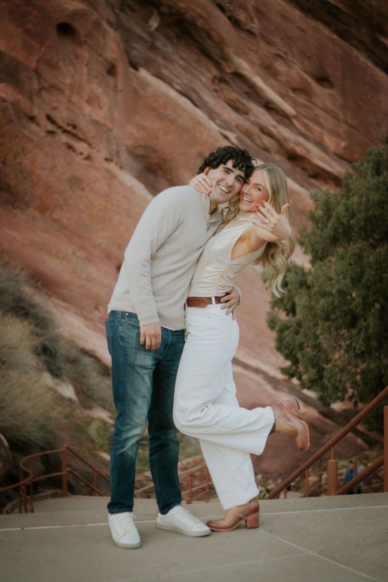 A couple shares a joyful moment together against dramatic red rock formations at an outdoor venue.