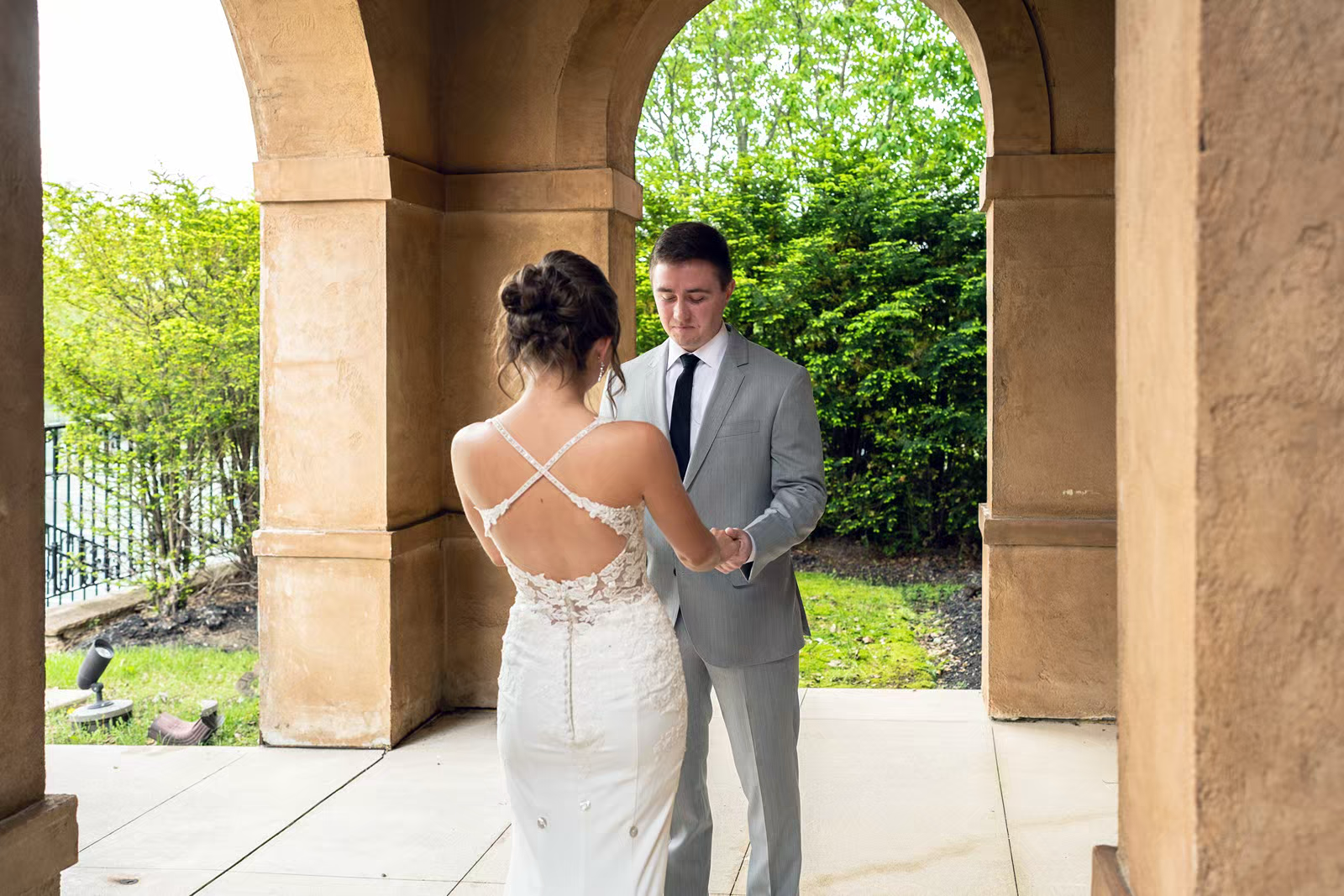 A couple stands beneath stone archways in a garden setting during their wedding ceremony.