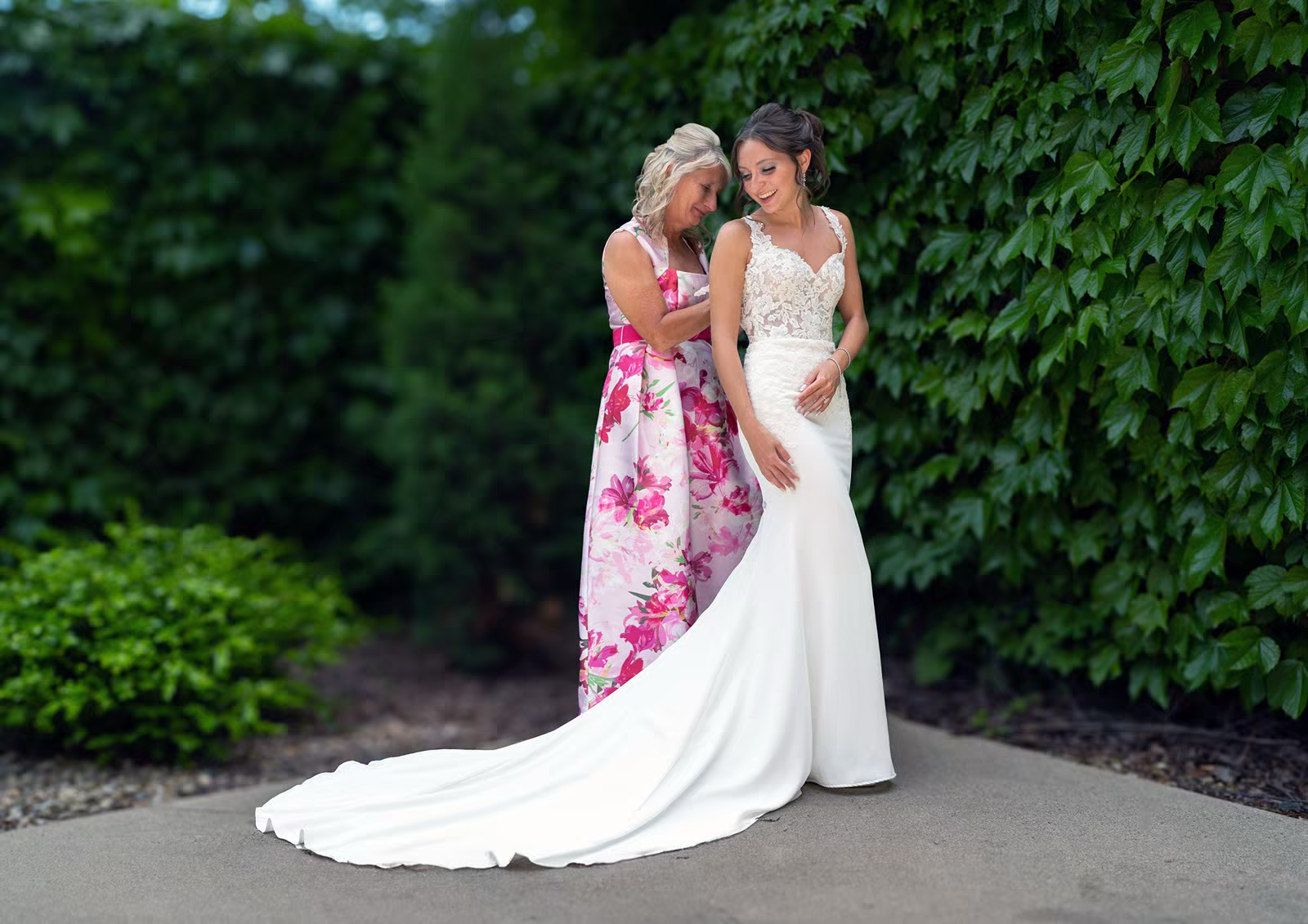A tender moment between two people in formal attire standing near lush green foliage in a garden setting.