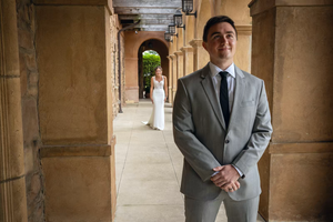 A person in a gray suit stands in an ornate stone archway corridor with warm lighting and classical architecture.