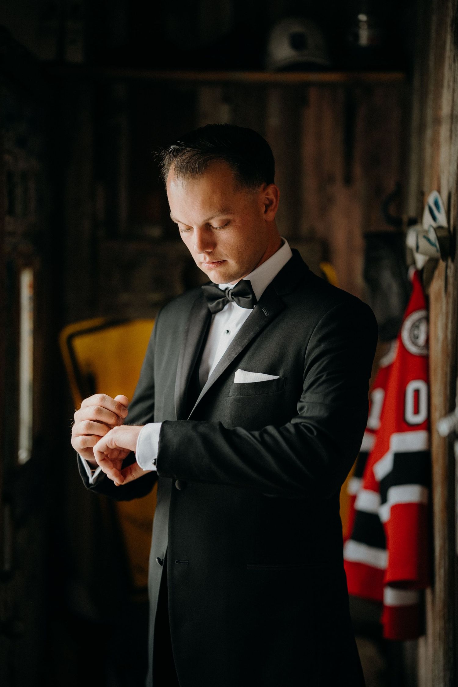 Young boy in formal black suit adjusts his tie while standing in front of red and white sports jerseys.