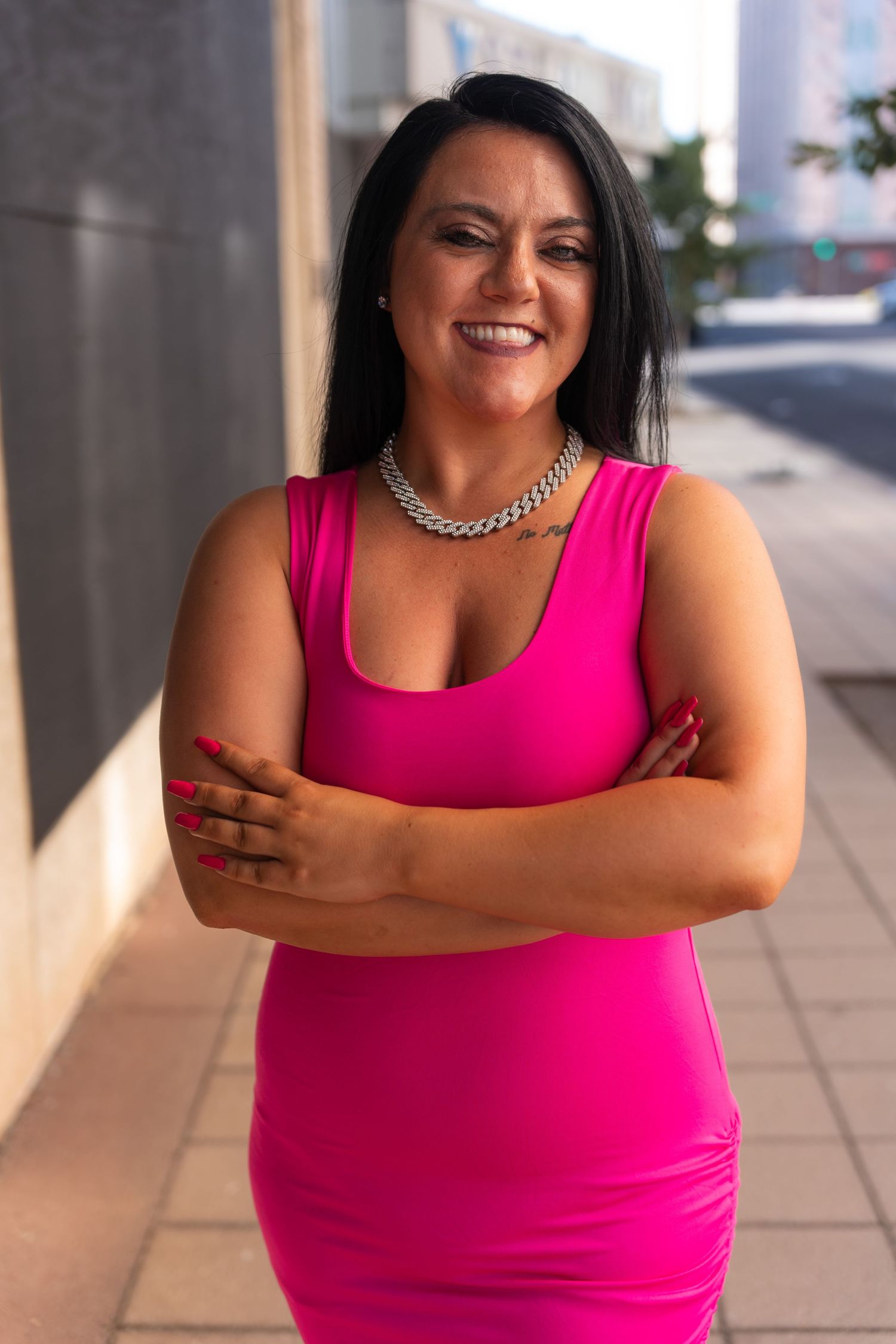 Confident poses in bright pink tank top against urban concrete background.