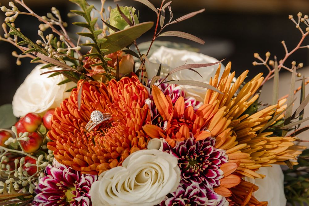 Vibrant autumn floral arrangement featuring orange chrysanthemums, burgundy dahlias, and white roses in warm lighting.