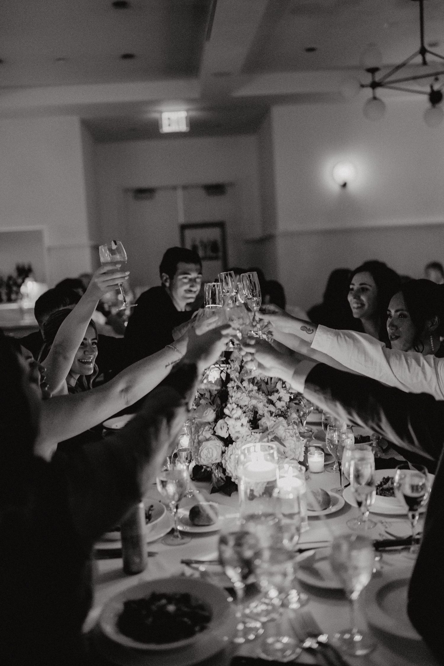 A group of people raise their glasses in a toast at an elegant dinner reception with candlelit tables.