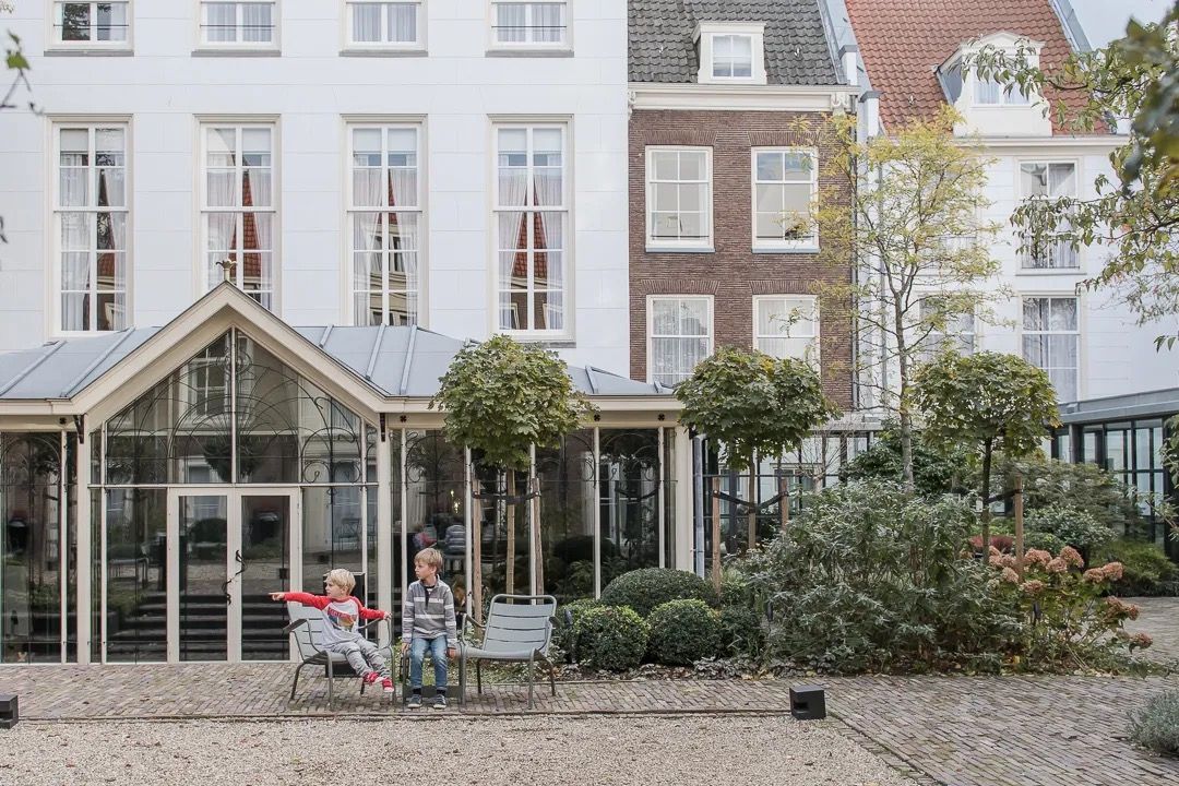 Family outside a large historic Amsterdam building with a glass entrance and garden.