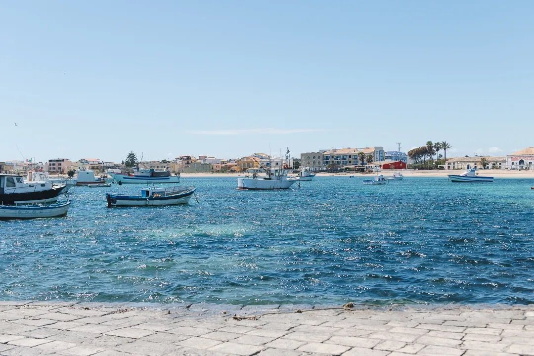 Small boats float on vivid blue water with a coastal town visible across the shoreline.