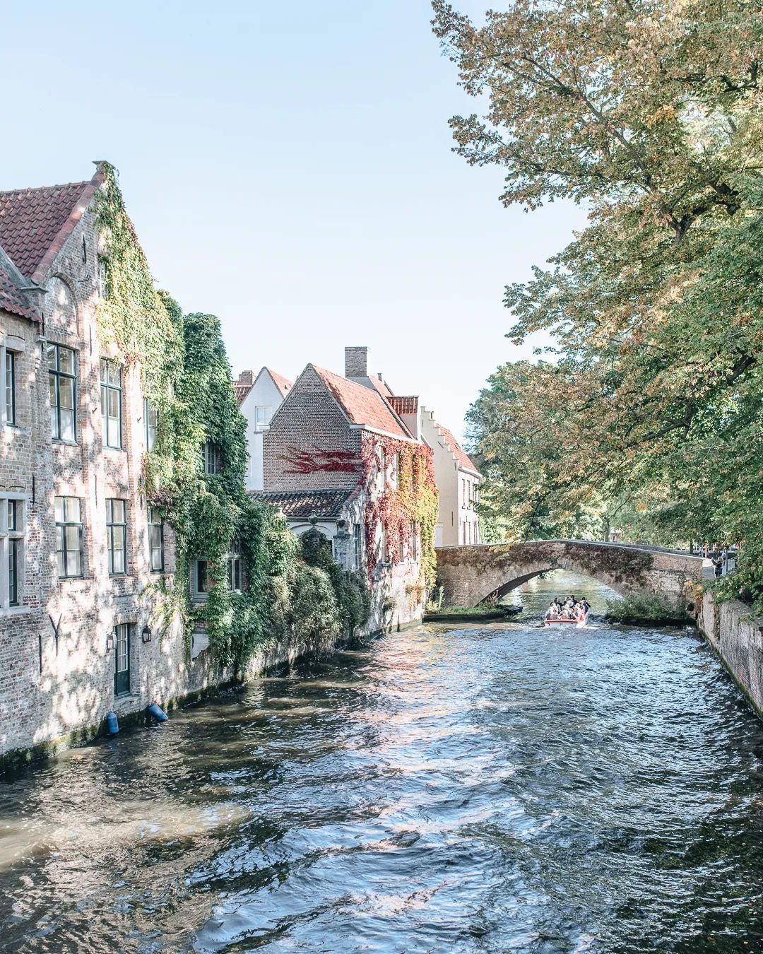 Shaded river flowing between old stone buildings and trees.